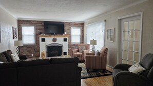A living room with a fireplace, a television, and two armchairs.