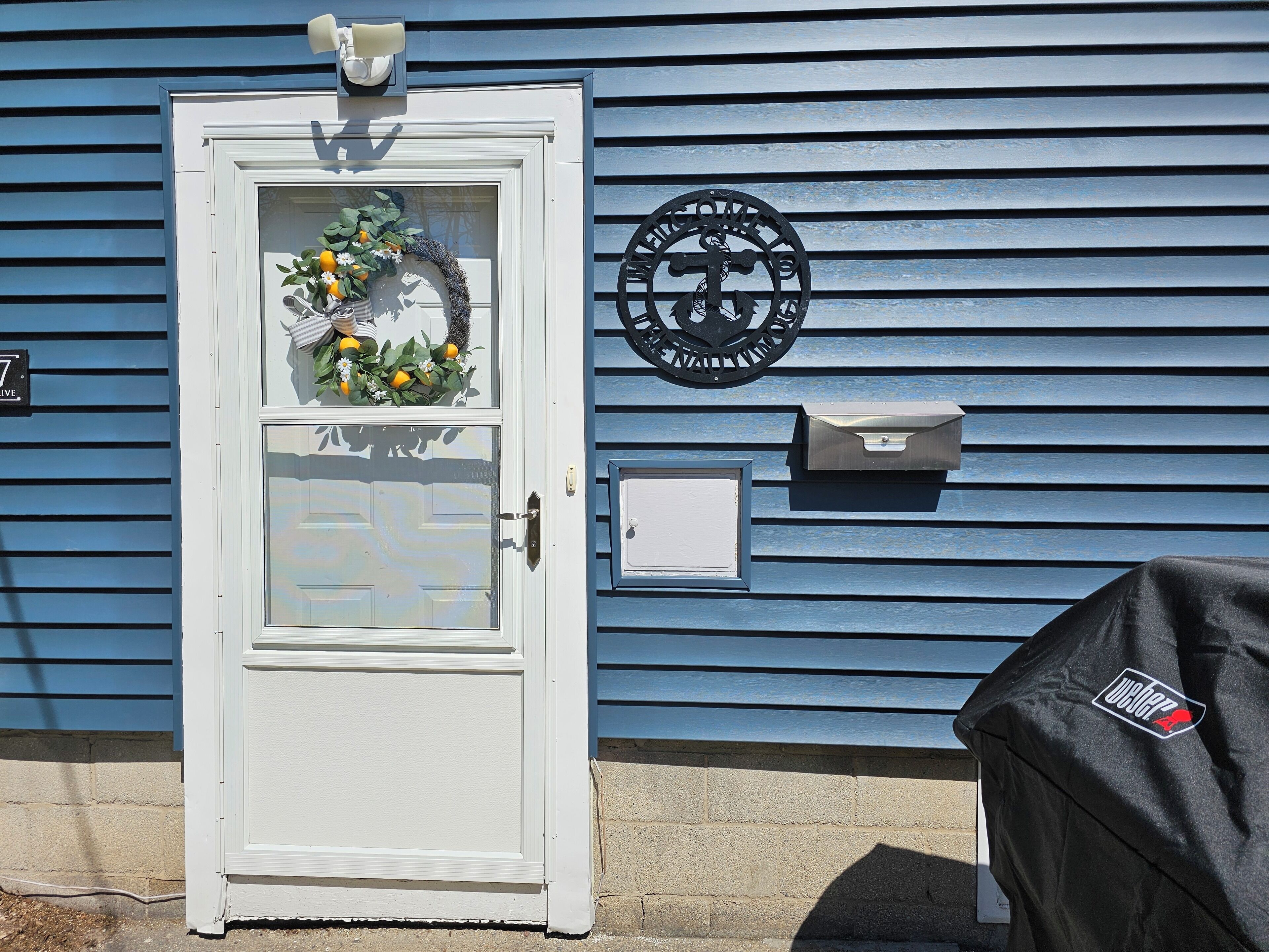 A white door with a wreath, a mailbox, and a welcome sign on a blue house.