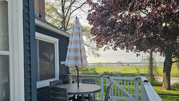 A deck with a table and chairs, an umbrella, and a view of a green field and water.