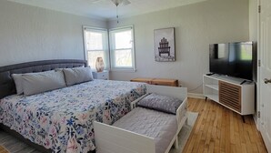 A bedroom with a large bed, a ceiling fan, a TV, and a window with blinds.