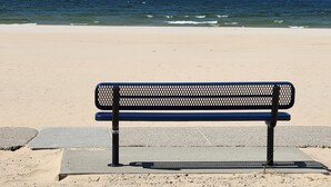 A bench on a sandy beach with the ocean in the background.