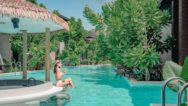 Un espace piscine doté d’un jacuzzi, entouré d’une végétation luxuriante et abrité par une structure à toit de chaume.
