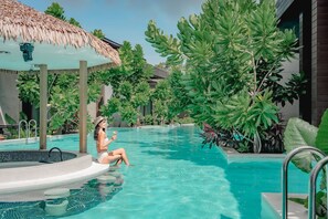 Ein Poolbereich mit Whirlpool, umgeben von üppiger Vegetation und einer Struktur mit Reetdach.