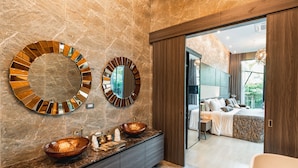 Une salle de bain moderne avec un grand miroir, deux vasques et une porte en bois donnant sur une chambre.