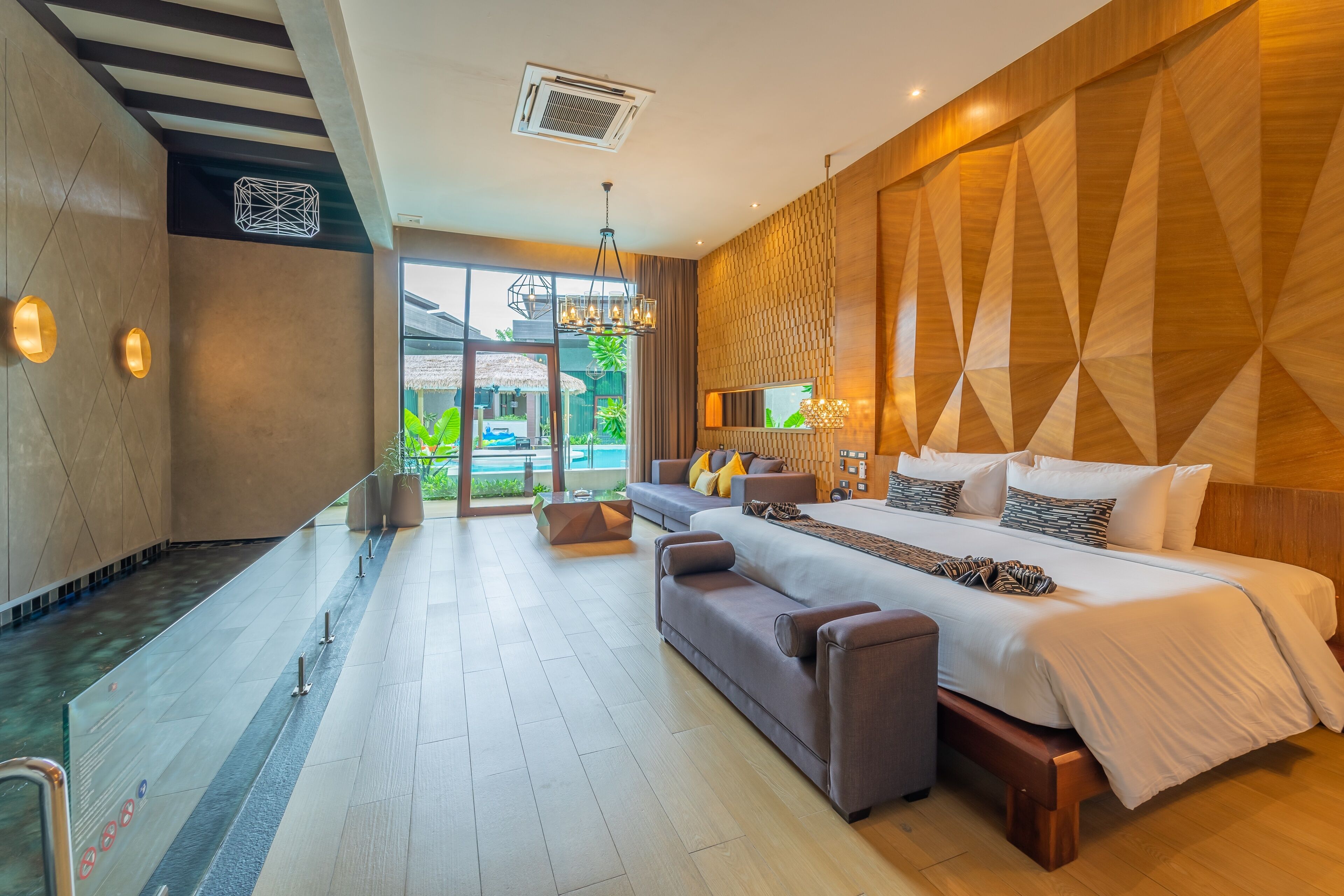 A modern hotel room with a large bed, a sofa, and a glass-enclosed bathroom.