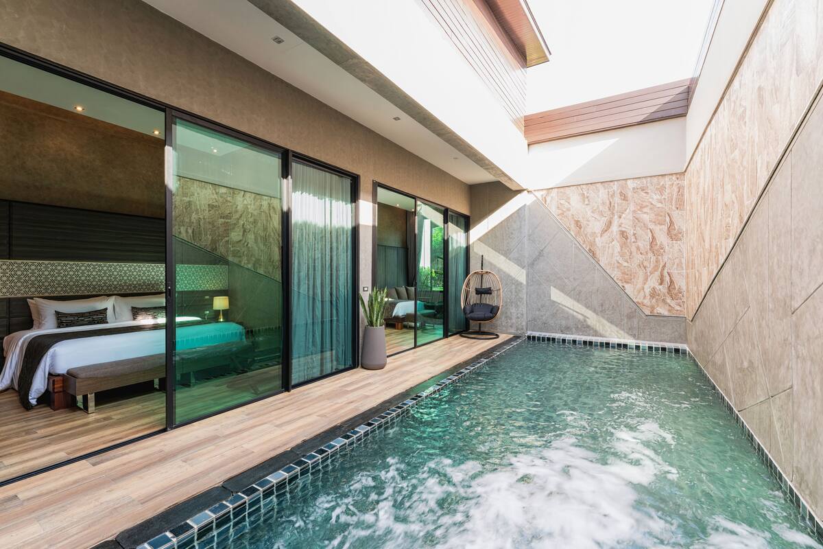 Een moderne hotelkamer met een glazen balkon, een klein zwembad en een gezellige zithoek met een hangstoel.