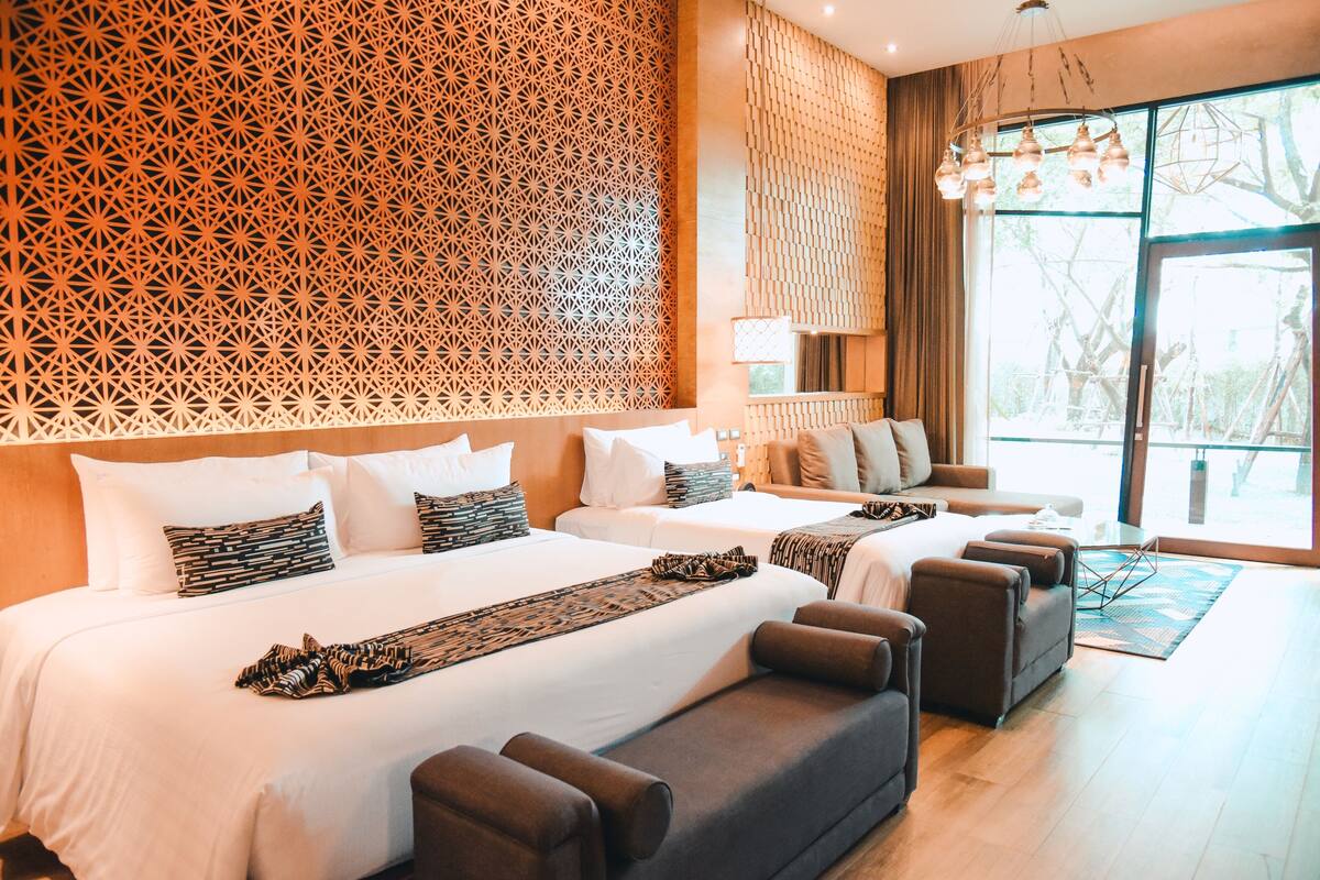 Een hotelkamer met twee bedden, een bank, een decoratieve wand, een groot raam en een kroonluchter.