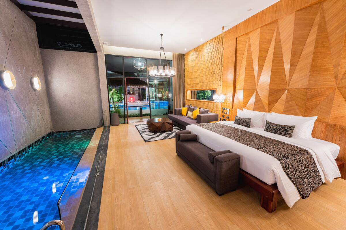Een moderne hotelkamer met een groot bed, een bank, een klein tafeltje en een zwembad dat in de kamer is geïntegreerd.