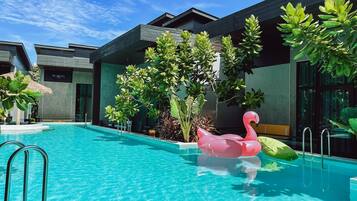 A swimming pool with a pink flamingo float, surrounded by modern buildings and lush greenery.