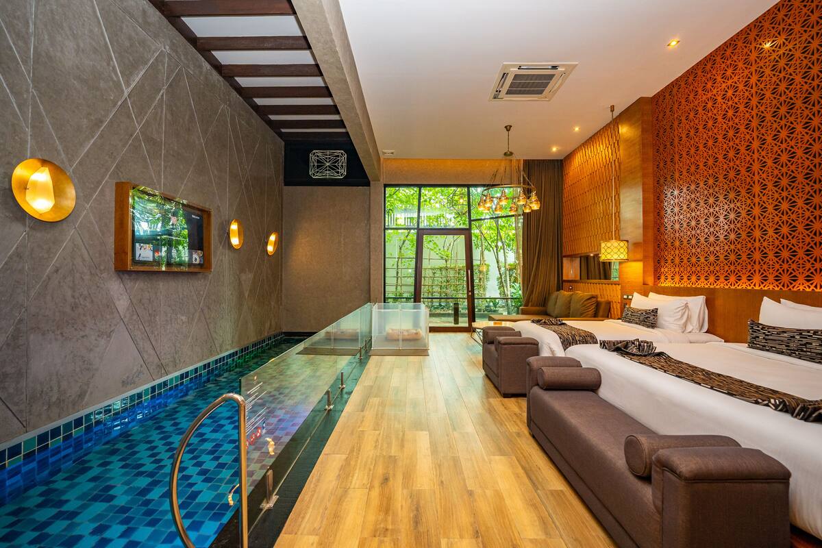 Een moderne hotelkamer met een glazen zwembad, een sofa, een bed en uitzicht op groen.
