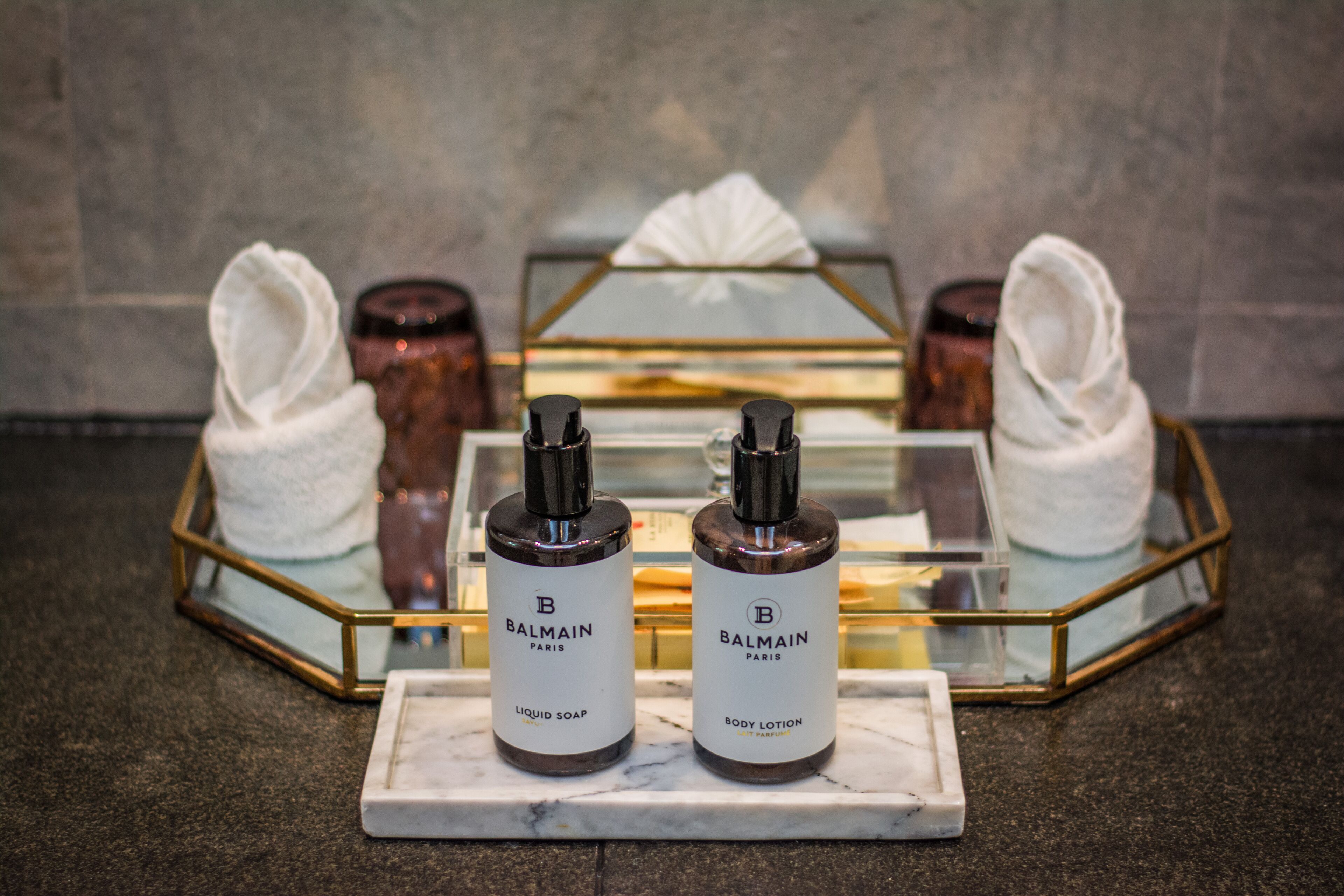 Two Balmain Paris body lotion bottles on a marble tray with a glass display case in the background.