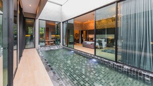Une piscine intérieure moderne avec des murs en verre, un sol carrelé et un coin salon confortable avec un canapé et une table basse.
