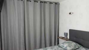 Ein Schlafzimmer mit einem Bett, grauen Vorhängen, einem Nachttisch mit Lampe und einer Wand mit dezentem Muster.