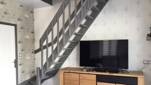 Ein modernes Wohnzimmer mit einem Holzkabinett, einem Flachbildfernseher und einer Treppe.