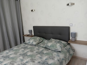 A bedroom with a bed, two bedside tables, a nightstand, a lamp, and a power outlet.