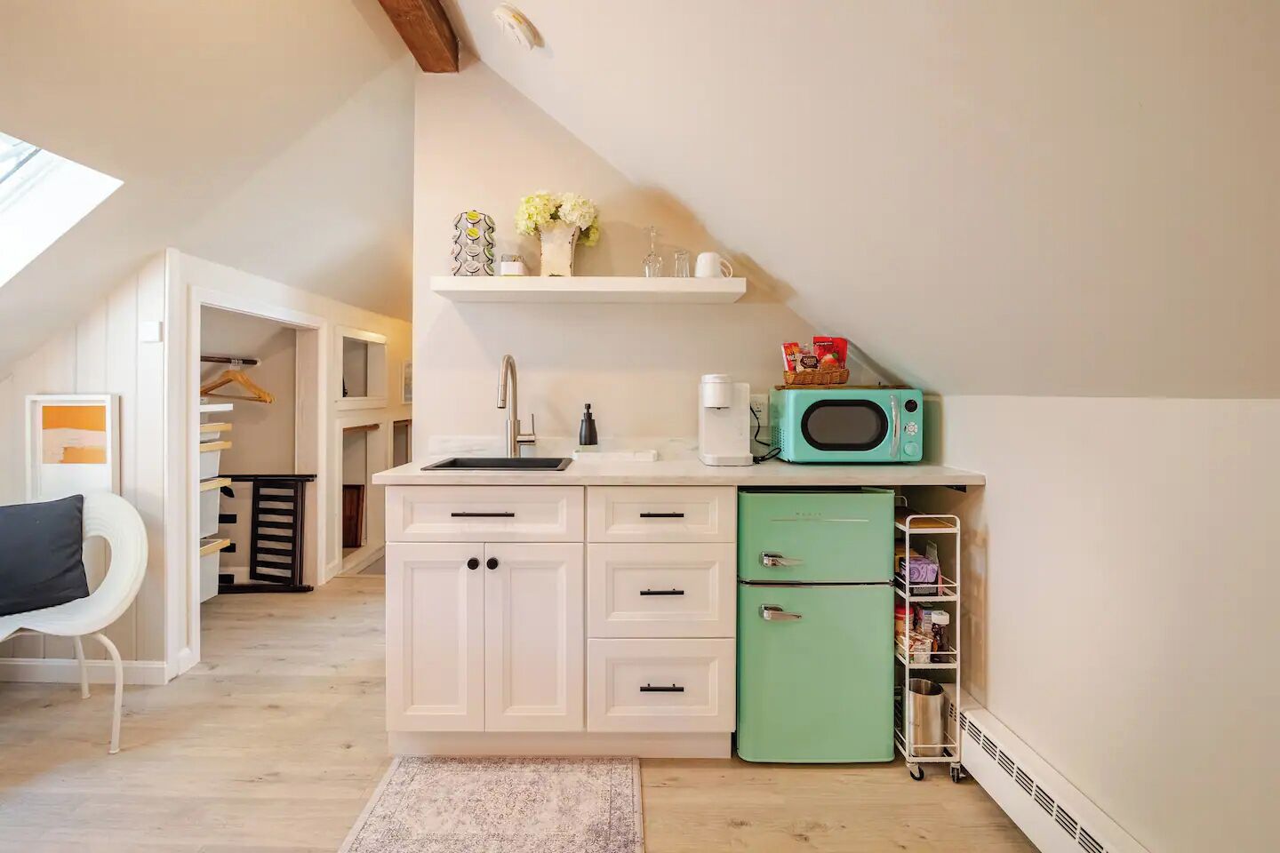 Cocina compacta con armarios blancos, un refrigerador verde, un microondas y un lavamanos.