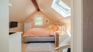 Camera da letto mansardata accogliente con un letto, una toeletta con specchio, una televisione e una finestra vista verde.