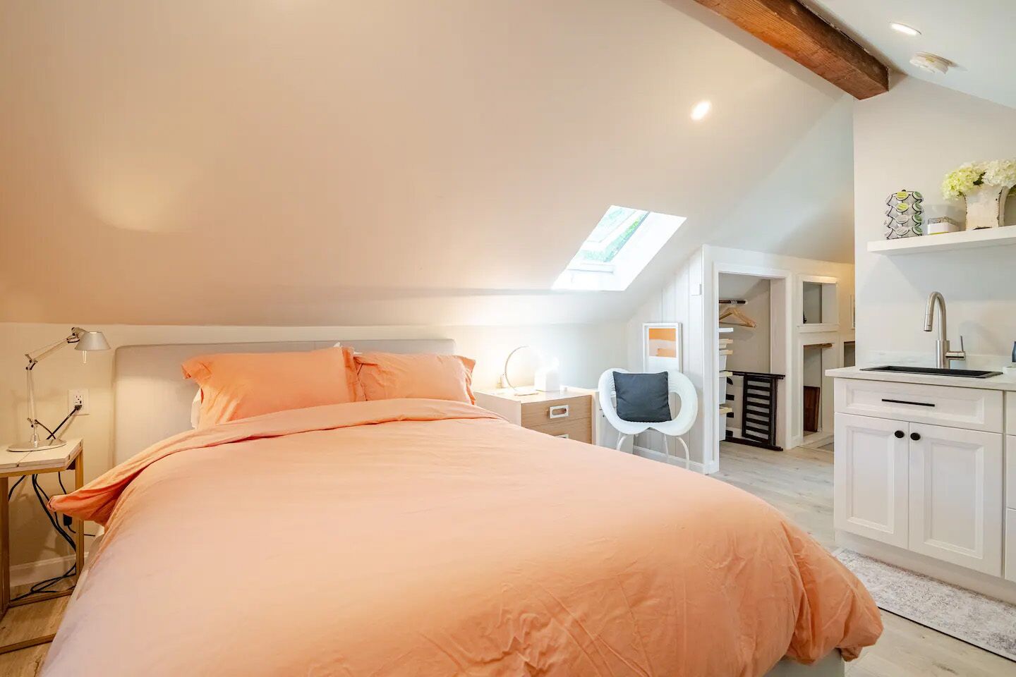Quarto com cama grande, escrivaninha, cadeira, claraboia e uma cozinha compacta.
