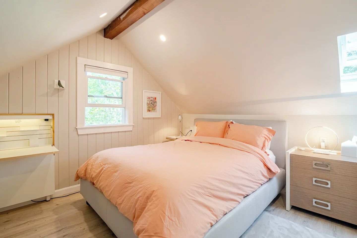 A bedroom with a bed, a bedside table, a lamp, a window, and a wall-mounted shelf.