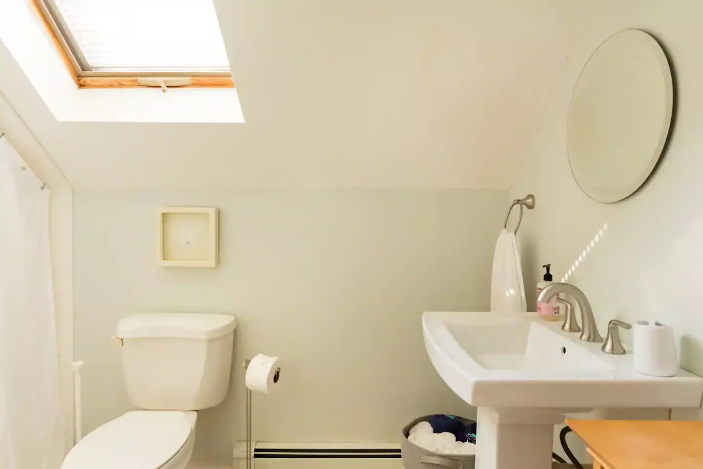 A bathroom with a skylight, toilet, sink, and a small mirror.