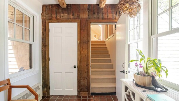 Un interno in legno con una porta bianca, una scala e una finestra con piante.
