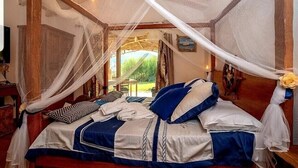Un dormitorio con cama cubierta por un dosel, cabecero de madera y vistas al exterior.