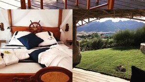 Una terraza de madera con una mesa y sillas, una cama con temática náutica y vistas a un paisaje verde.