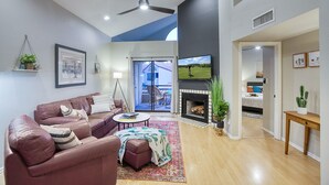 A modern living room with a leather sofa, a coffee table, and a fireplace. There is a television mounted on the wall and a ceiling fan. - Scottsdale - Boho Cactus Condo - Newly Renovated! (Paradise Valley)
