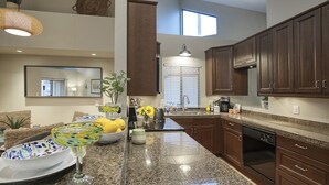 A modern kitchen with dark wooden cabinets, granite countertops, and a large island. There is a window providing natural light and a ceiling light fixture. - Scottsdale - Boho Cactus Condo - Newly Renovated! (Paradise Valley)