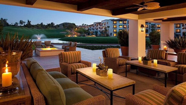 A cozy outdoor seating area with sofas and tables, a fire feature, and a view of a golf course and buildings in the background. - Scottsdale - Boho Cactus Condo - Newly Renovated! (Paradise Valley)