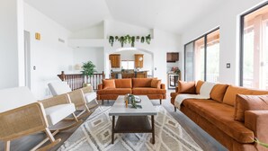 A modern living room with a sofa, chairs, and a coffee table. There is a kitchen in the background with wooden cabinets and a window. - Amazing Peaceful Resort - Heated Pool, Hot Tub (Fountain Hills)