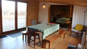 Een eethoek met een tafel gedekt voor twee personen, houten banken, een gele stoel en uitzicht door een glazen deur op het buiten.