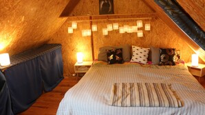 Een gezellig slaapkamer onder de dakpannen, met een bed met gestreepte lakens, meerdere kussens en wandlampen.