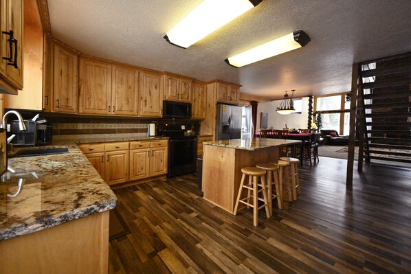A kitchen with wooden cabinets, granite countertops, a stainless steel refrigerator, and a bar area with stools.