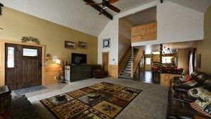 A spacious living room with a large sectional sofa, a wooden staircase, and a cozy fireplace. - Mountain View Cabin 22 Miles From Yellowstone (Island Park)