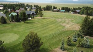 A large, well-maintained grassy area with several buildings, likely a resort or lodge, surrounded by trees and distant mountains. - Mountain View Cabin 22 Miles From Yellowstone (Island Park)