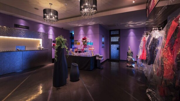 Un moderno vestíbulo de hotel con una recepción, una planta decorativa y una exhibición de trajes.