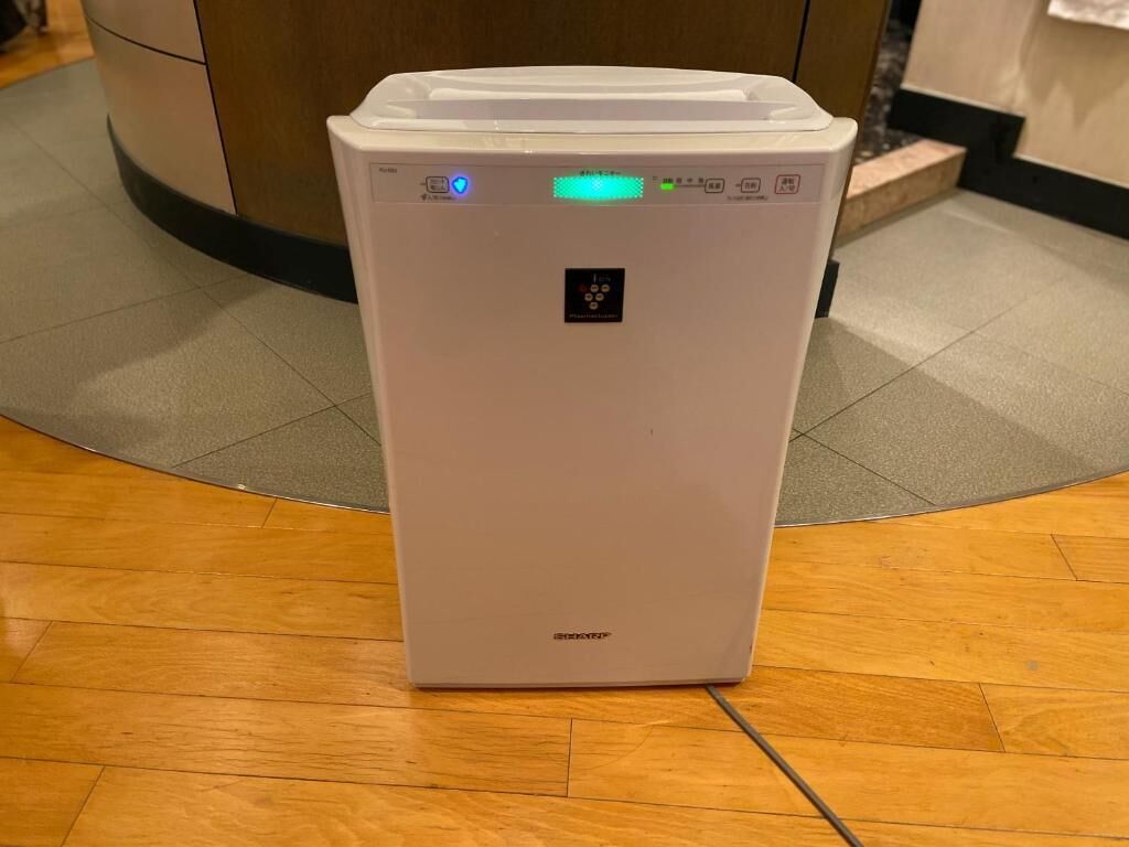 Un calentador portátil blanco con pantalla digital y botones de control, sobre un piso de madera.
