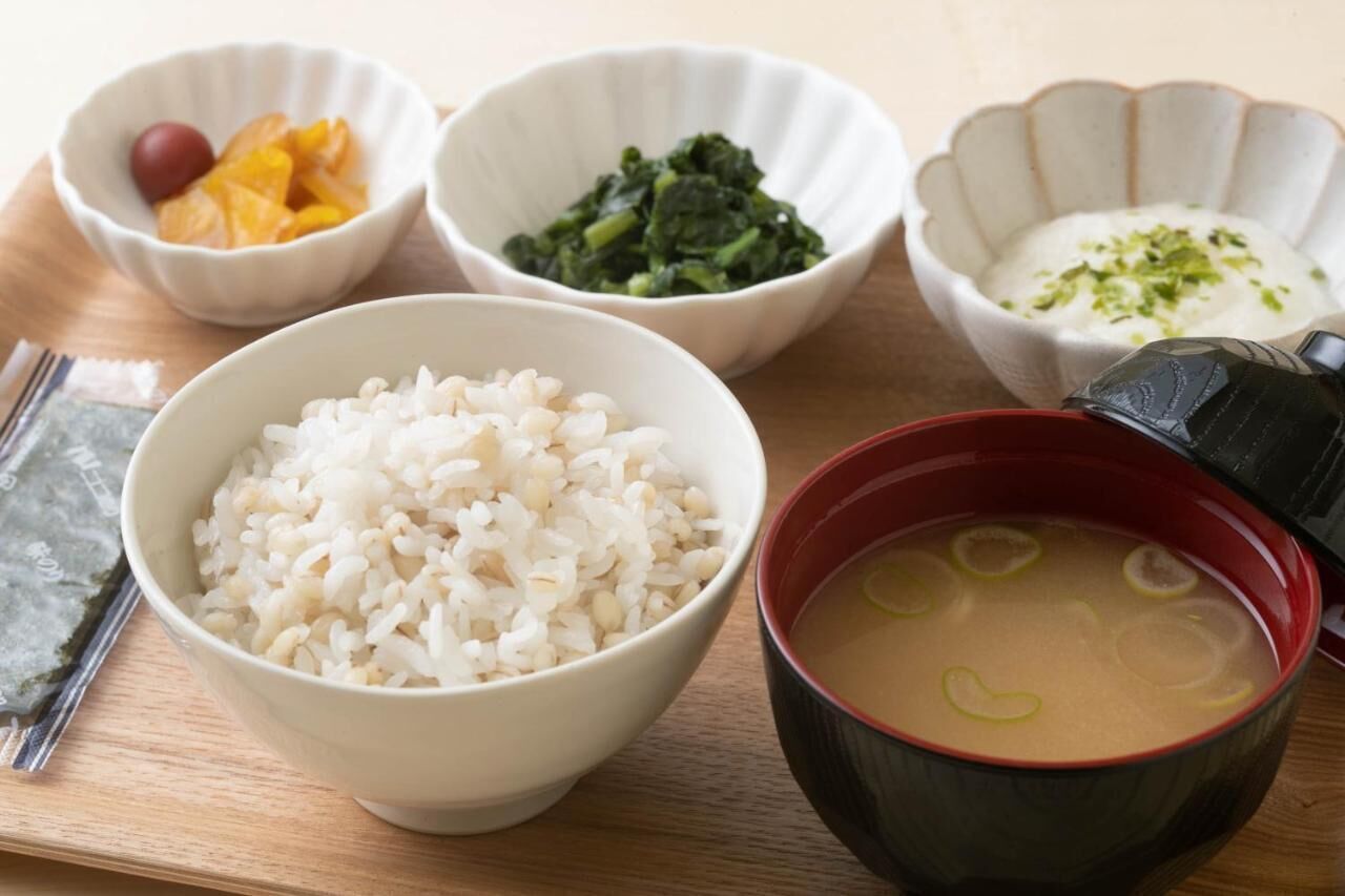 A table with bowls of rice, pickled vegetables, spinach, a creamy dish, and a soup with lemon slices.