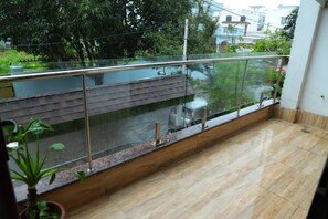 A balcony with a glass railing, a tiled floor, and a view of a street with trees and buildings. - Awesome Property Someone Will Love To Live (Rishikesh)