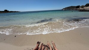 A beach with clear water, a sandy shore, and a person’s legs in the foreground. - Oceanview Deluxe Penthouse Apartment With 89m2 Living Space & 90m2 Roof Terrace (Okrug)