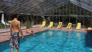 Una piscina con copertura in vetro, circondata da sdraio e alcune persone.