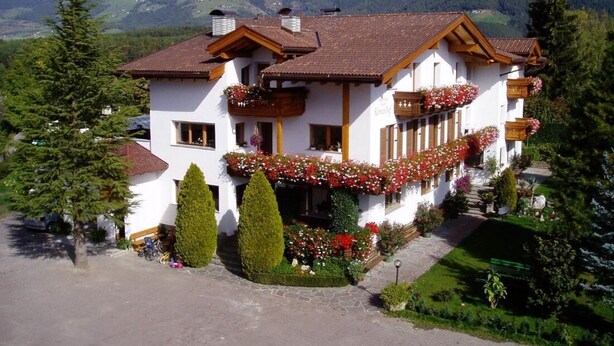 Un edificio bianco con tetto marrone, immerso nel verde e affiancato da montagne.