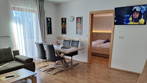Un soggiorno moderno con un divano, un tavolo da pranzo con sedie, una TV e un letto sullo sfondo.
