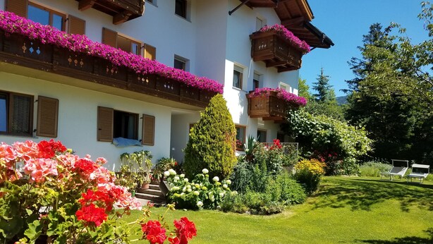 A white building with wooden balconies, a well-maintained garden, and a clear sky. - Residence Klementhof #1 (Naz Sciaves)