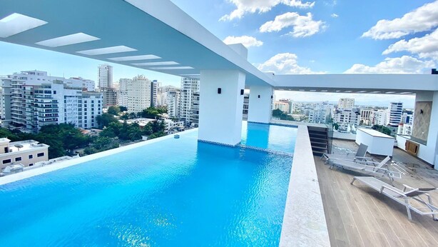 Piscina infinita en la azotea con vistas a la ciudad, rodeada de edificios modernos.