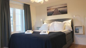A neatly made bed with white linens, a dark blue bedspread, and a headboard. There is a painting of a pier on the wall above the bed. - Casa Schilling 2,5 Rooms in St Gallen, Modern, Quiet and Close to the Center (St. Gallen)