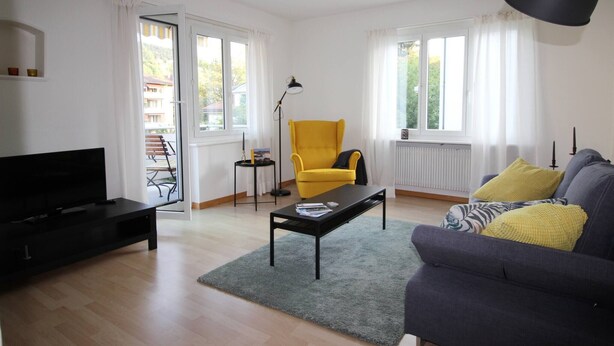 A living room with a sofa, a yellow armchair, a black coffee table, and a TV. - Casa Schilling- 2,5 Rooms With Balcony Near Hospital, University (St. Gallen)