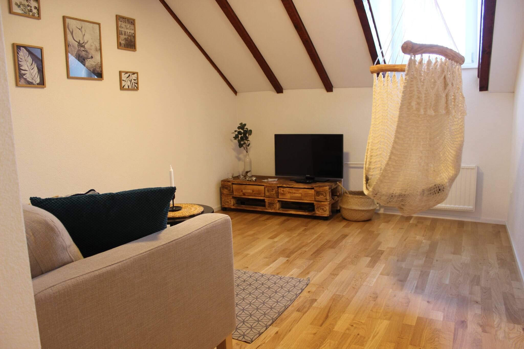 A living room with a sofa, a television, wooden flooring, and a ceiling with exposed beams.