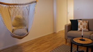 Une pièce avec un fauteuil suspendu, un canapé agrémenté de coussins à motifs, une petite table ronde avec une bougie et un tapis aux motifs géométriques.